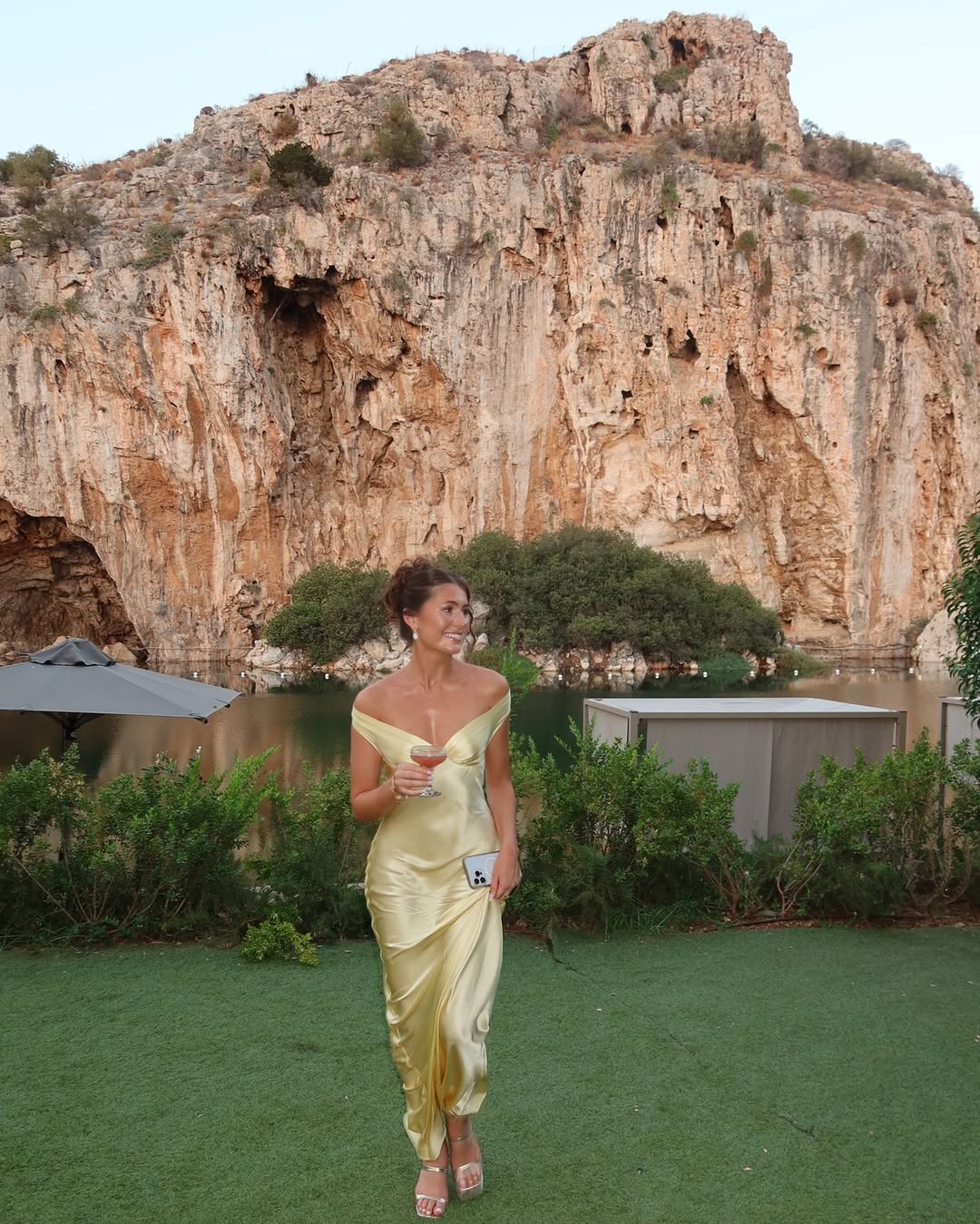 Woman in a yellow dress standing in front of a rocky cliff and body of water.