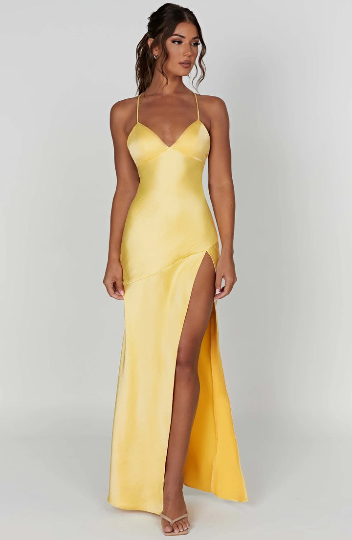 Woman wearing a yellow evening gown with a slit on a white background