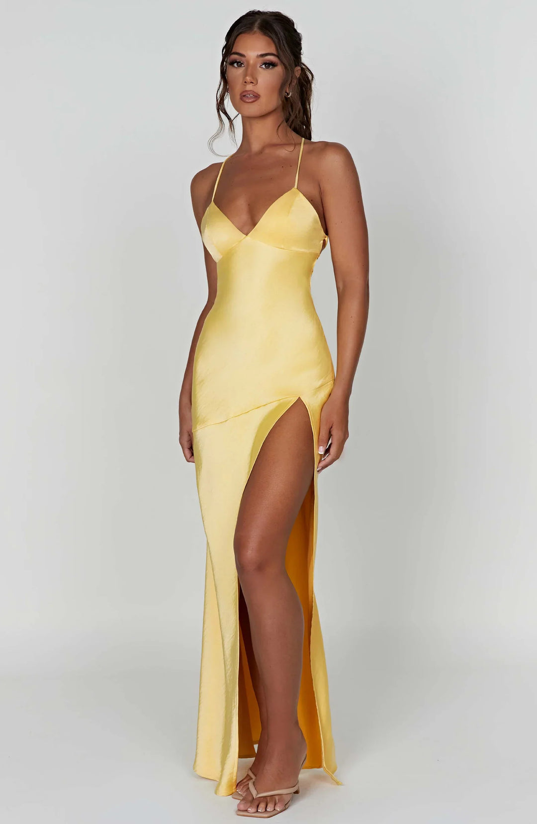 Woman wearing a yellow evening gown with a high slit on a white background