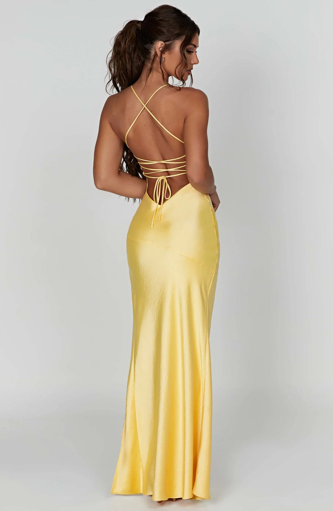 Woman wearing a yellow evening gown with a backless design on a white background
