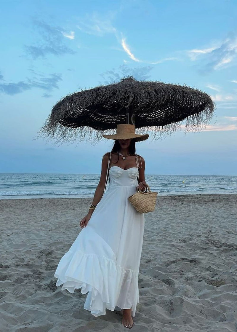 Woman in a white dress holding a large straw hat on a beach