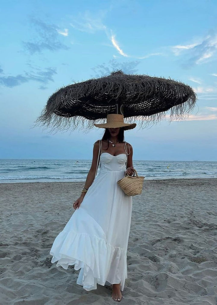 Woman in a white dress holding a large straw hat on a beach