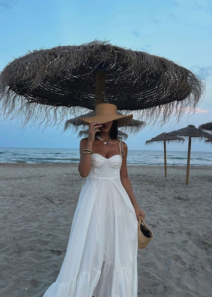 Woman in a white dress and large straw hat on a beach with ocean view
