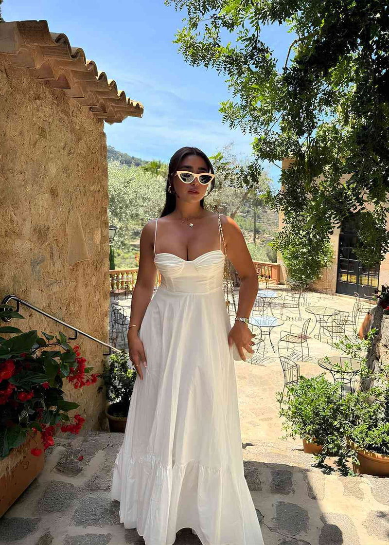 Woman in a white dress standing outdoors with greenery and a building in the background