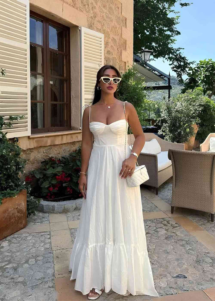 Woman in a white dress standing outdoors near a building with greenery.