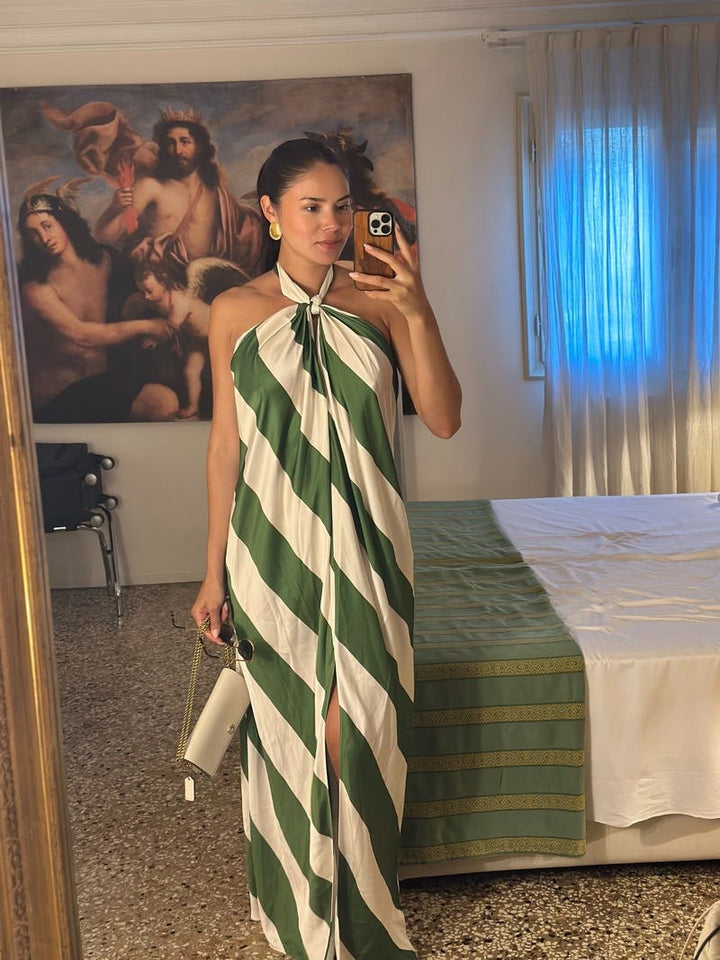 Woman taking a mirror selfie wearing a green and white striped dress in a room with a painting and bed in the background.