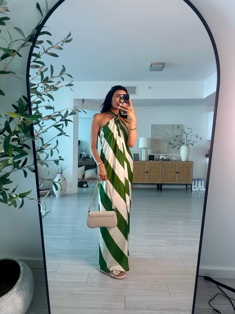 Woman taking a mirror selfie wearing a green and white striped dress in a modern living room.