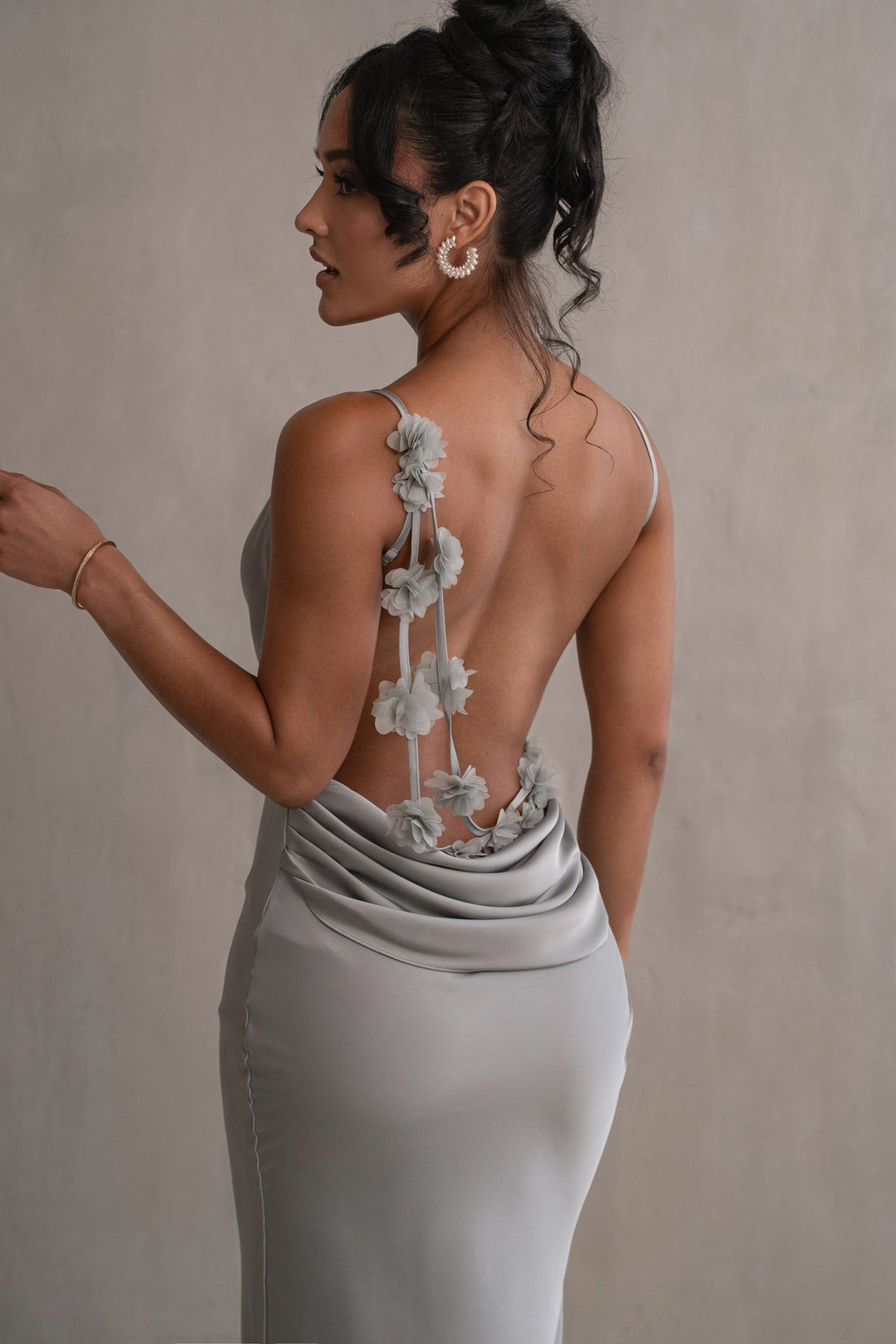 Woman wearing a silver gown with floral back design against a neutral background
