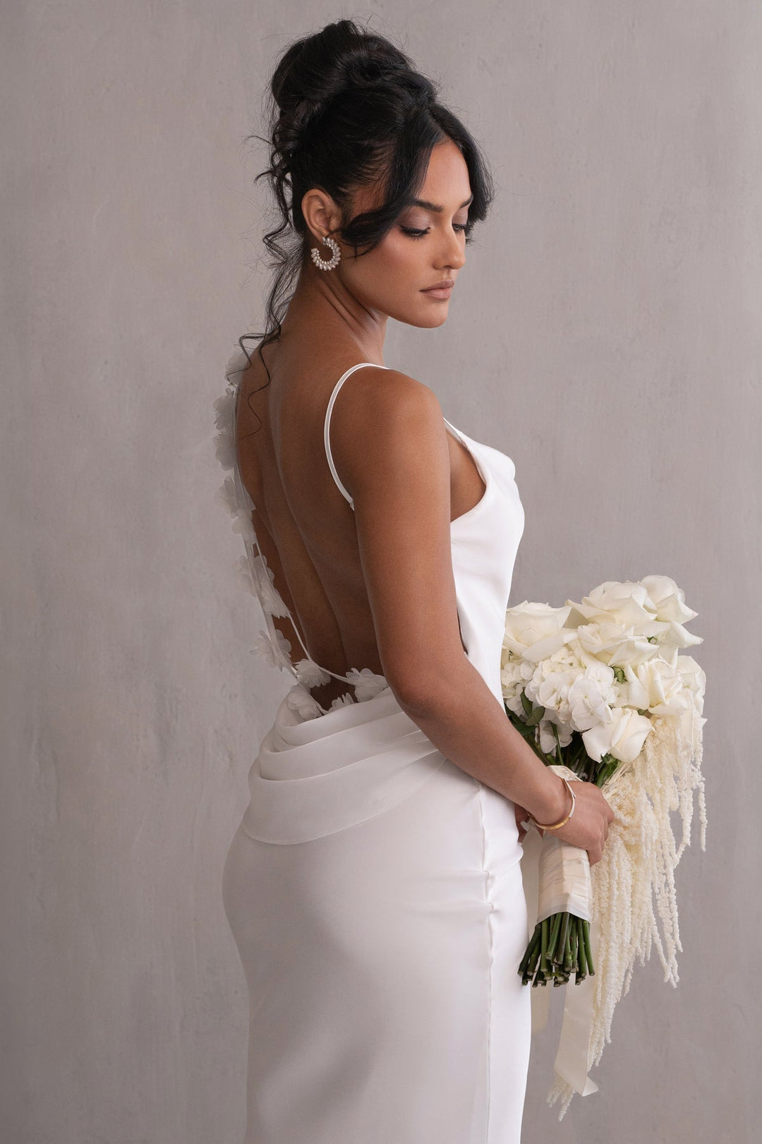 Woman in a white wedding dress holding a bouquet against a plain background
