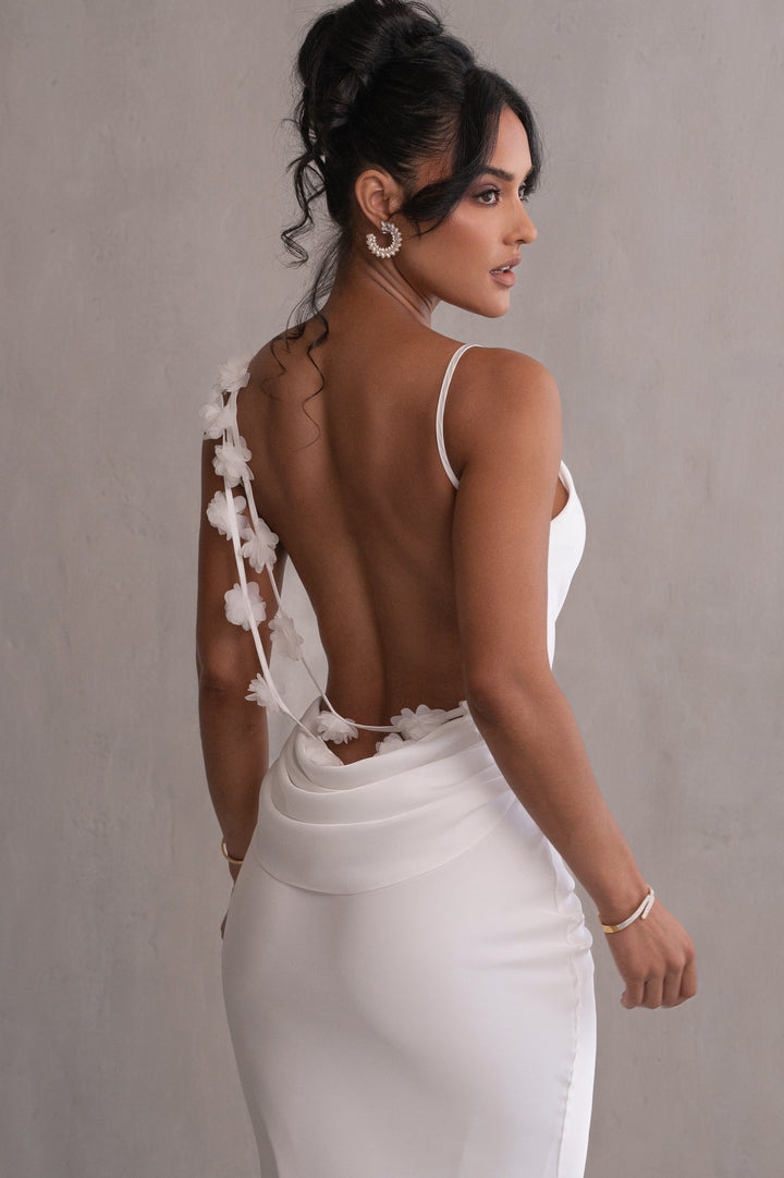 Woman wearing a white dress with floral details on a plain background