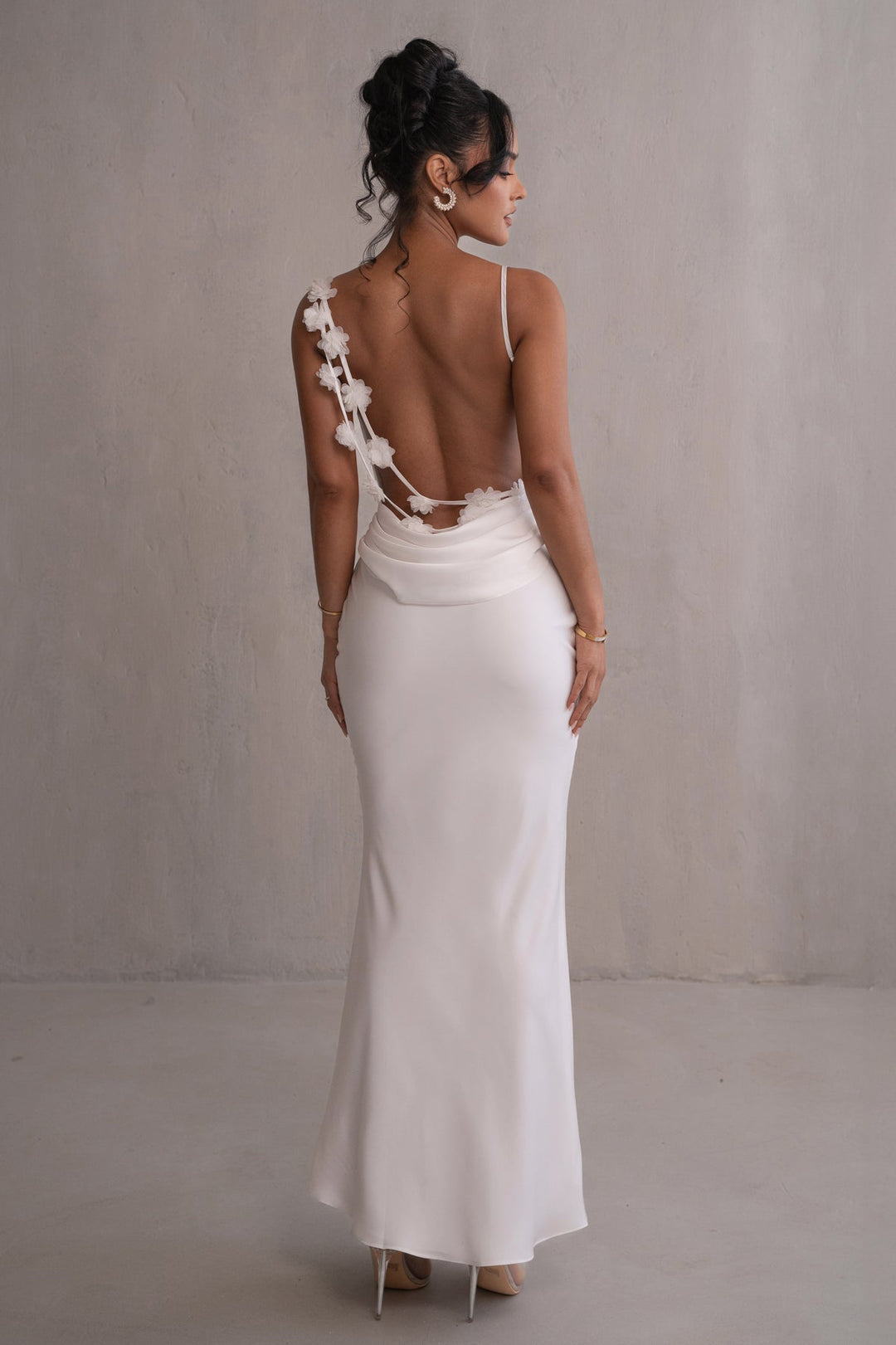 Woman wearing a white wedding dress with an open back against a neutral background
