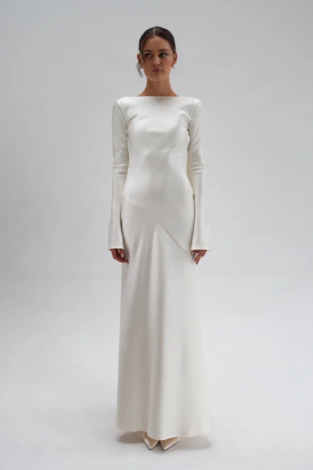 Woman wearing a long, elegant white dress against a plain background