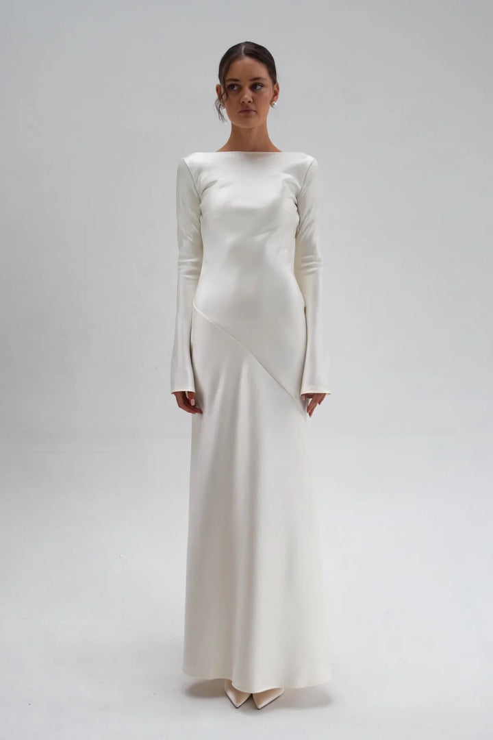 Woman wearing a long, elegant white dress against a plain background