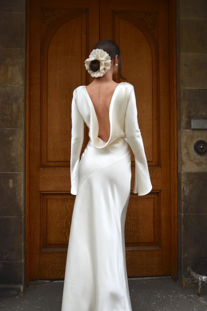 Woman in a white wedding dress with a low back standing in front of a wooden door.
