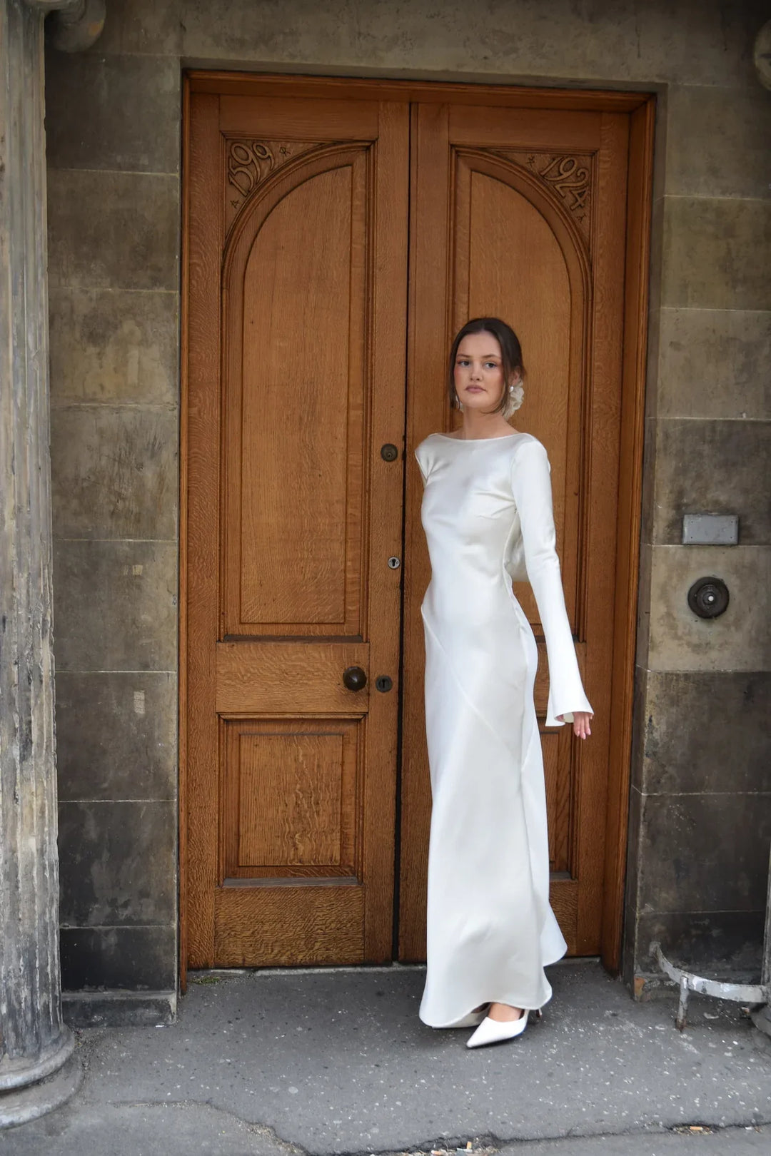 Woman in a white dress standing in front of a wooden door.
