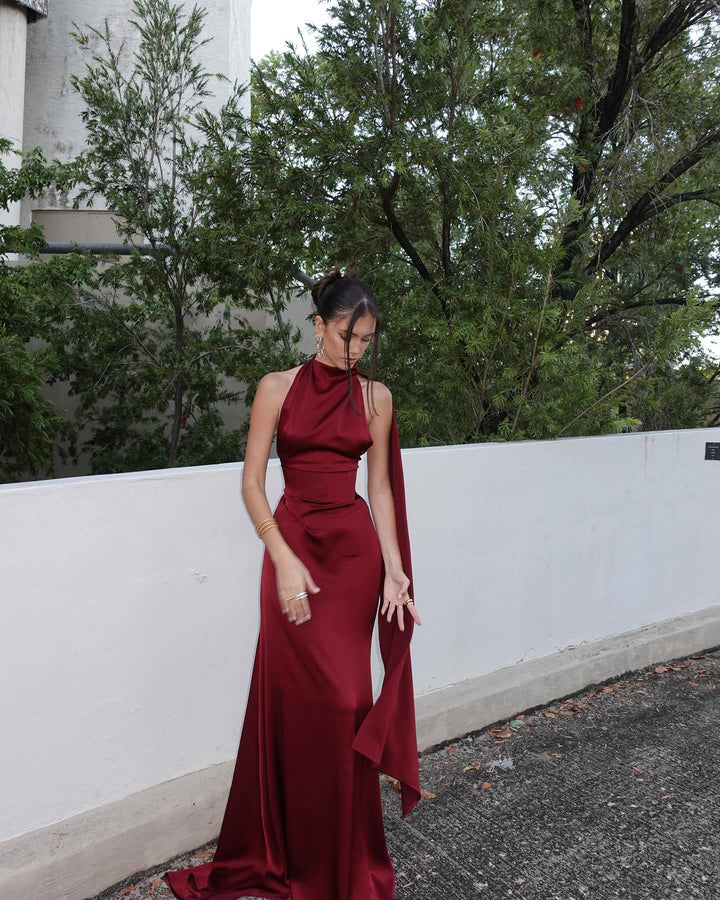 Woman in a burgundy evening gown standing outdoors with trees in the background