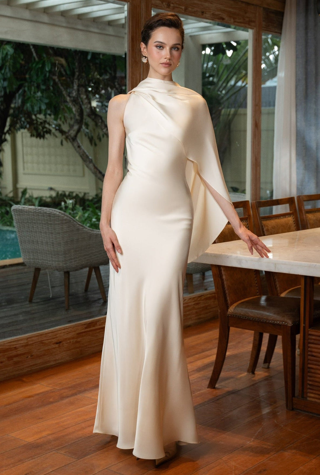 Woman in a white evening gown standing in a dining area.