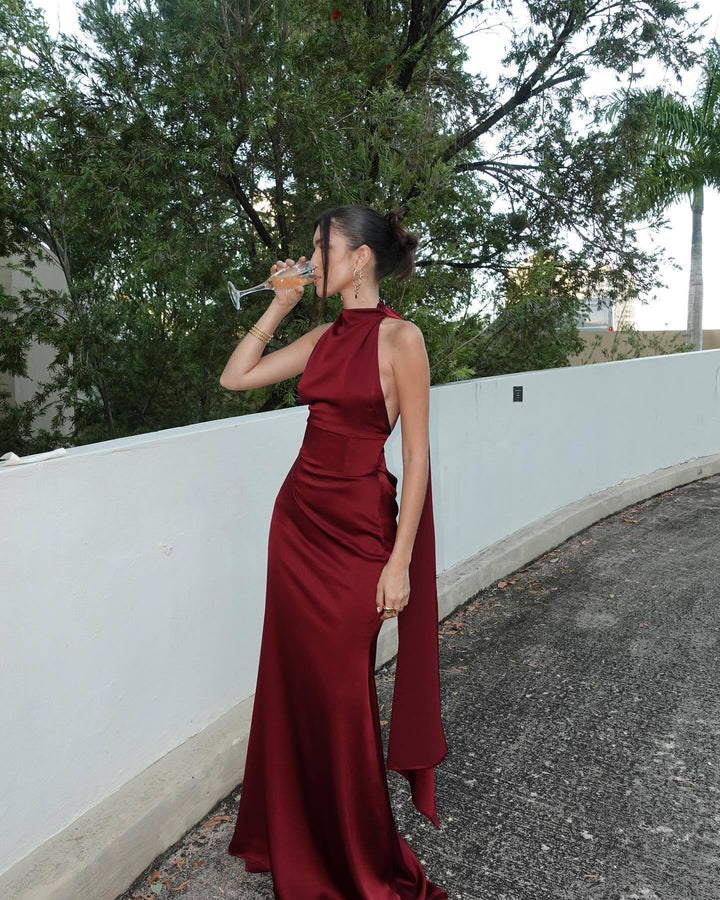 Woman in a burgundy dress drinking from a glass outdoors.