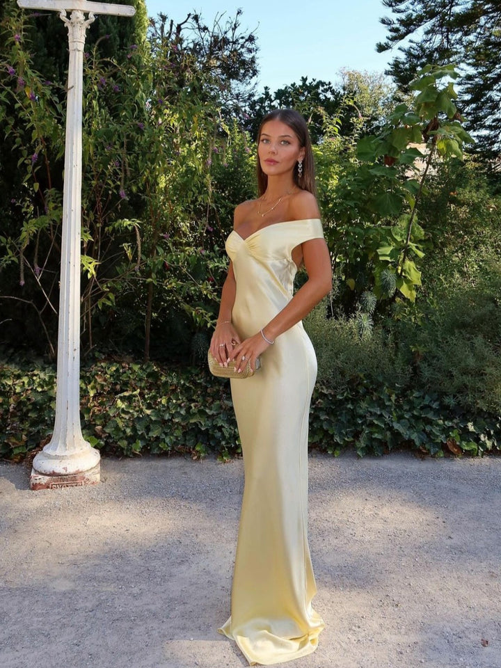 Woman in a yellow off-shoulder dress standing outdoors with greenery in the background