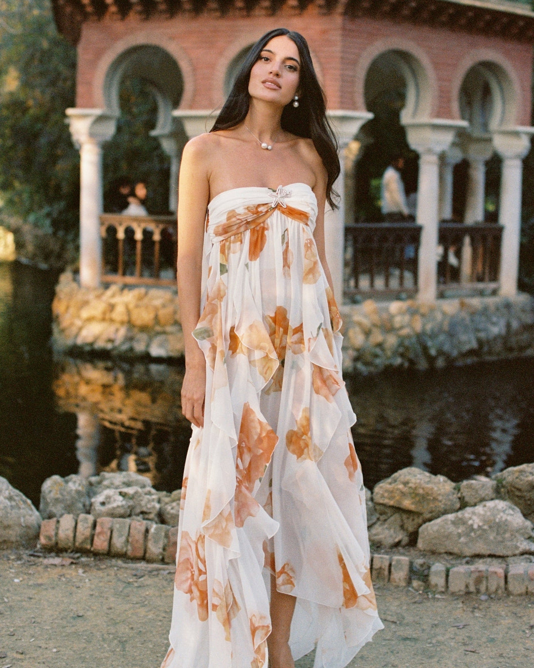 Woman in a strapless floral dress standing in front of a historic building with a pond.
