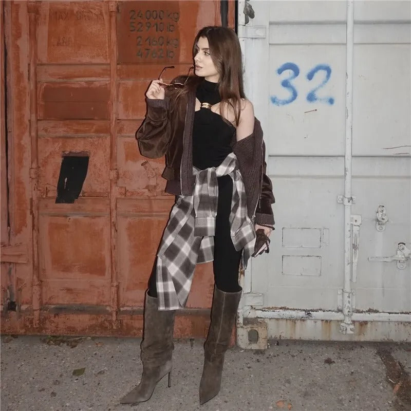 Woman in stylish outfit with plaid shirt and brown boots against a rustic background