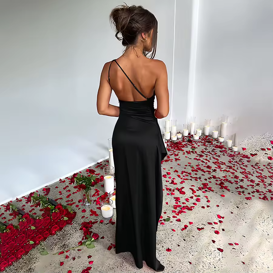 Woman in a black dress standing in a room with red rose petals and candles.