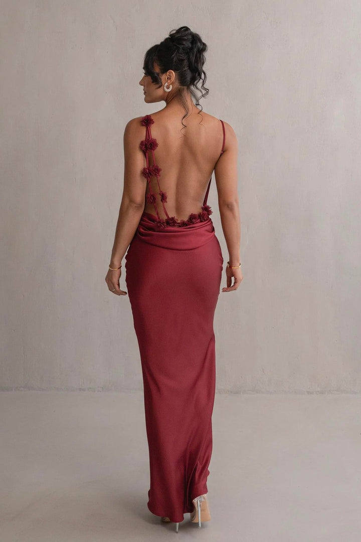 Woman wearing a burgundy evening gown with floral details on a plain background