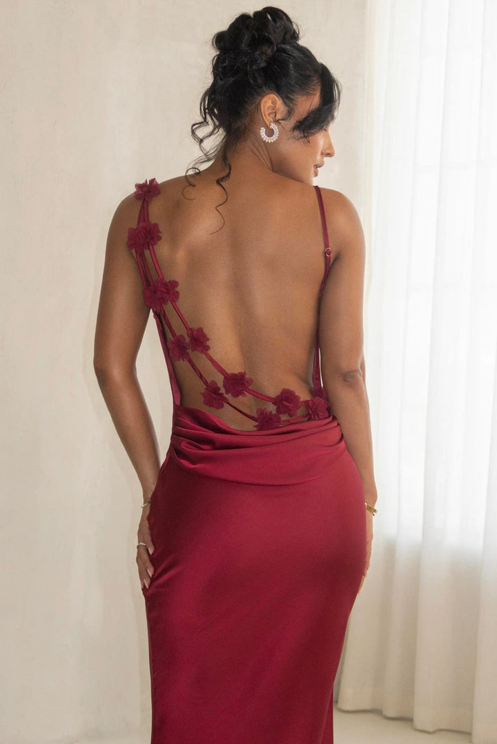 Woman wearing a burgundy evening gown with floral detailing in a softly lit room.