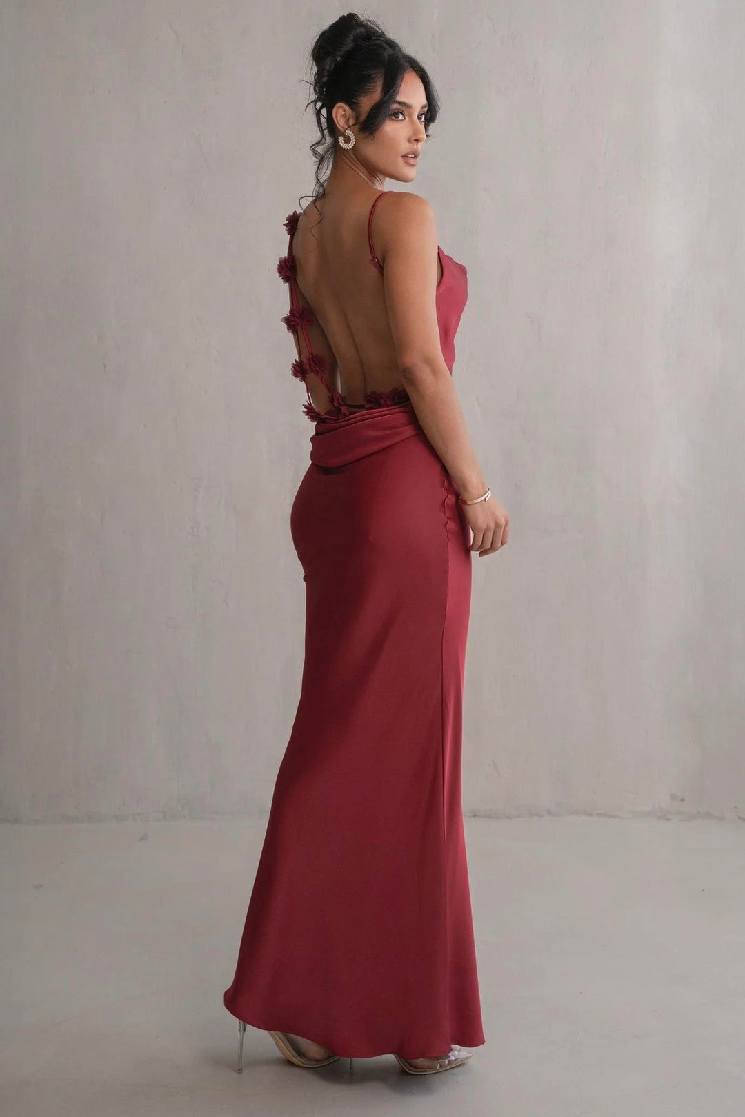 Woman wearing a red evening gown with floral details on a plain background