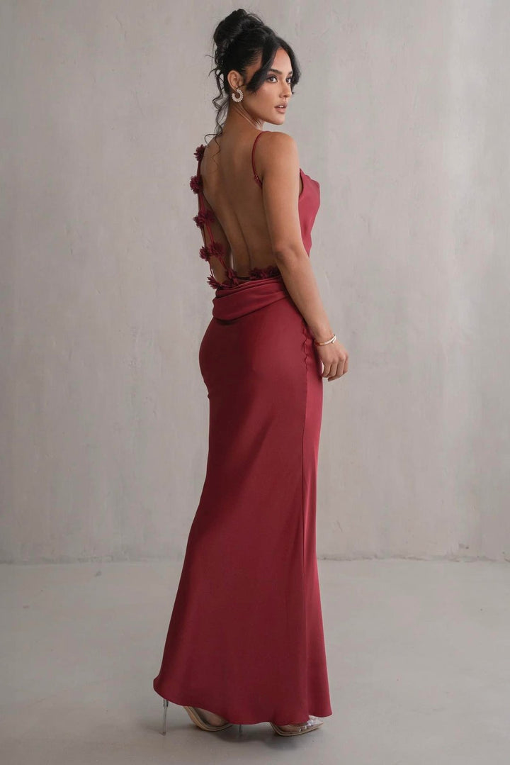 Woman wearing a red evening gown with floral details on a plain background