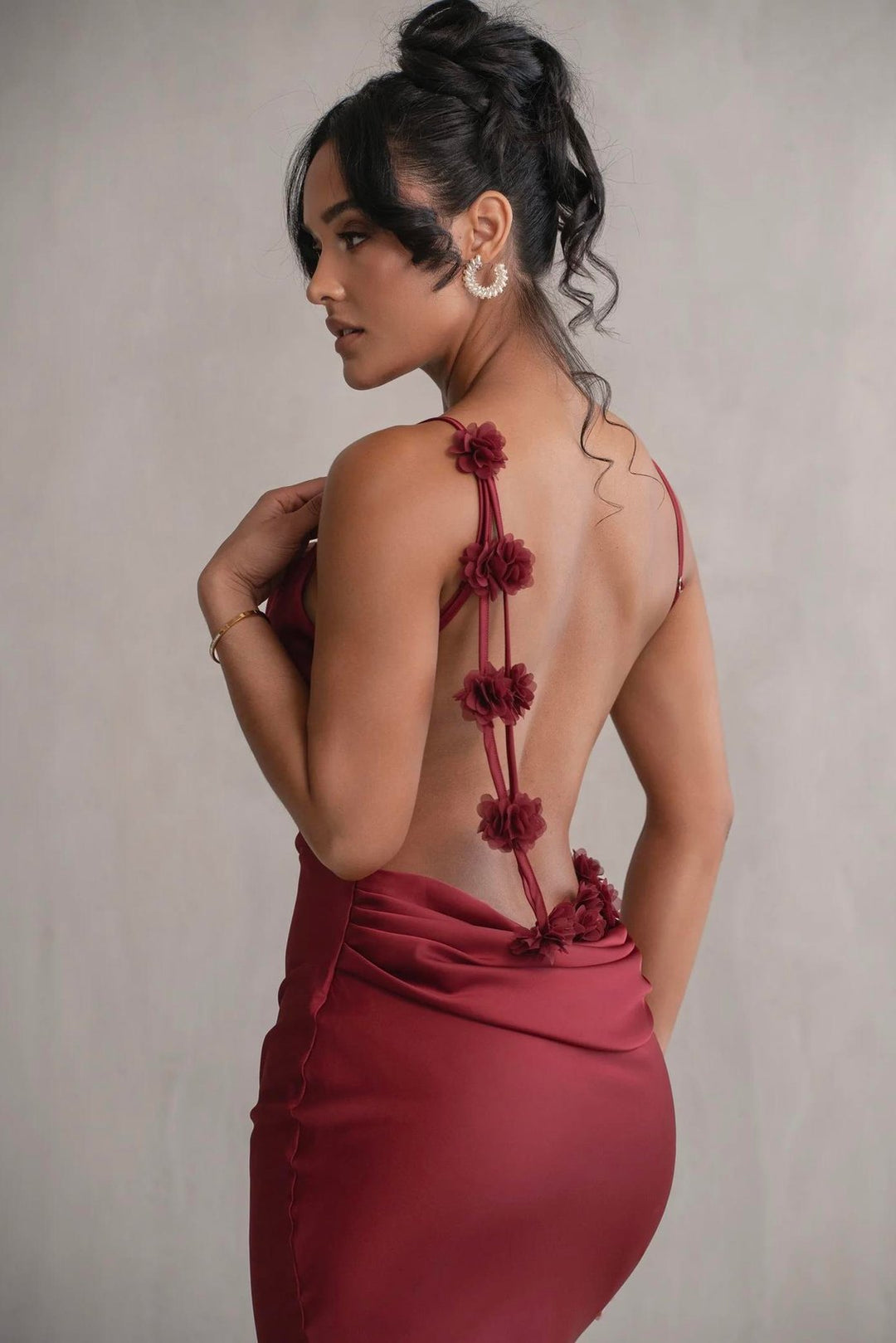 Woman wearing a burgundy dress with floral back design against a neutral background