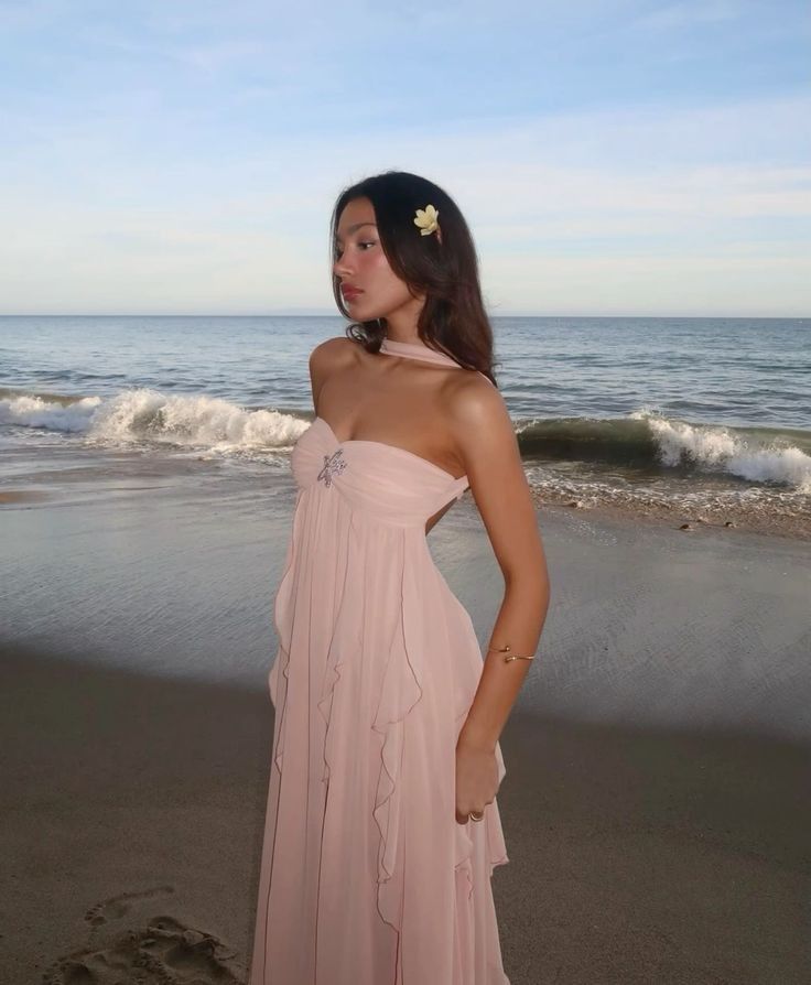Woman in a pink dress standing on a beach with waves in the background
