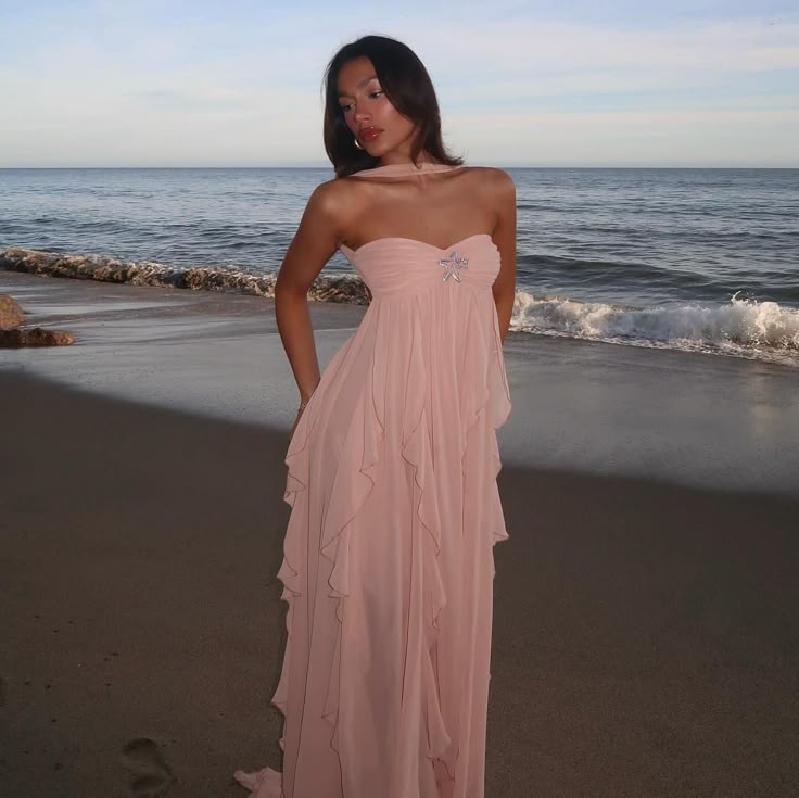 Woman in a pink dress standing on a beach with ocean waves in the background