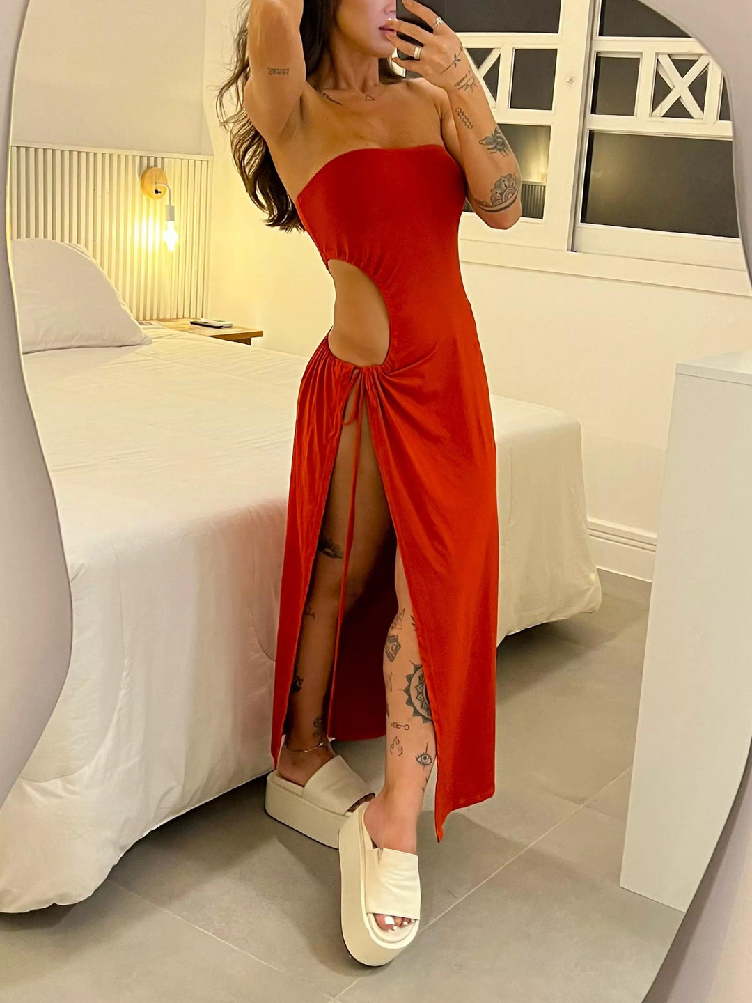 Woman in a red dress with cut-out design standing in a bedroom.