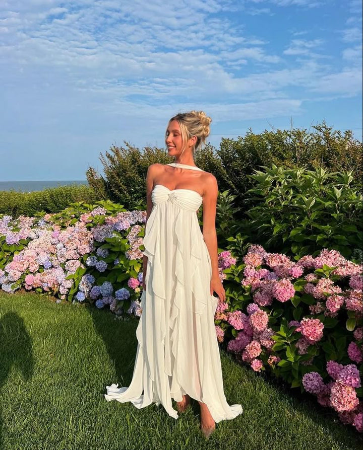 Woman in a white dress standing in a garden with pink and purple flowers and a blue sky.