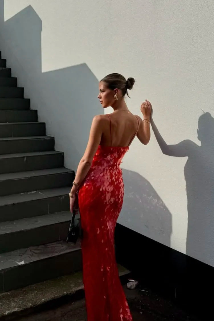 Woman in a red evening gown standing on a staircase with a white wall behind her.