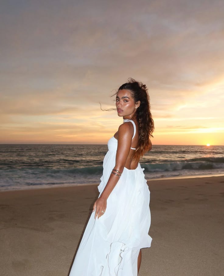 Woman in a white dress standing on a beach at sunset
