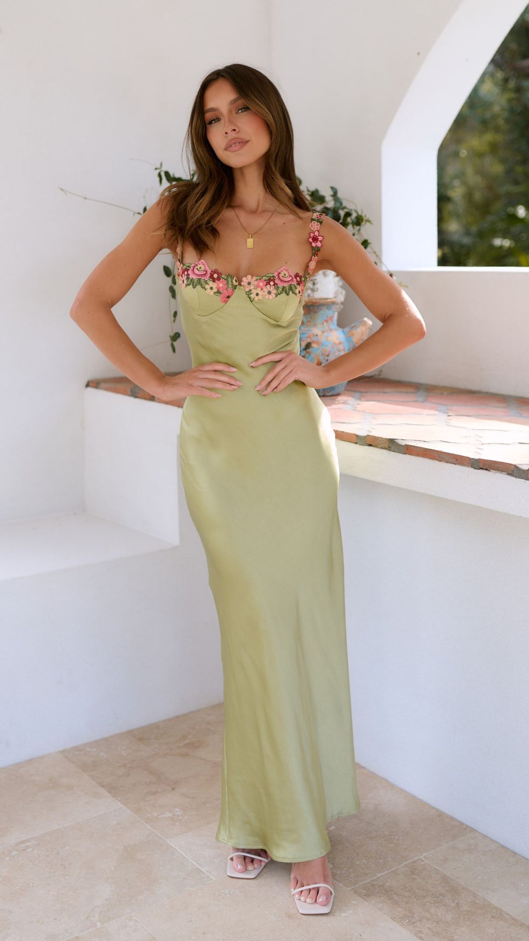 Woman wearing a light green dress with floral straps in a bright room.