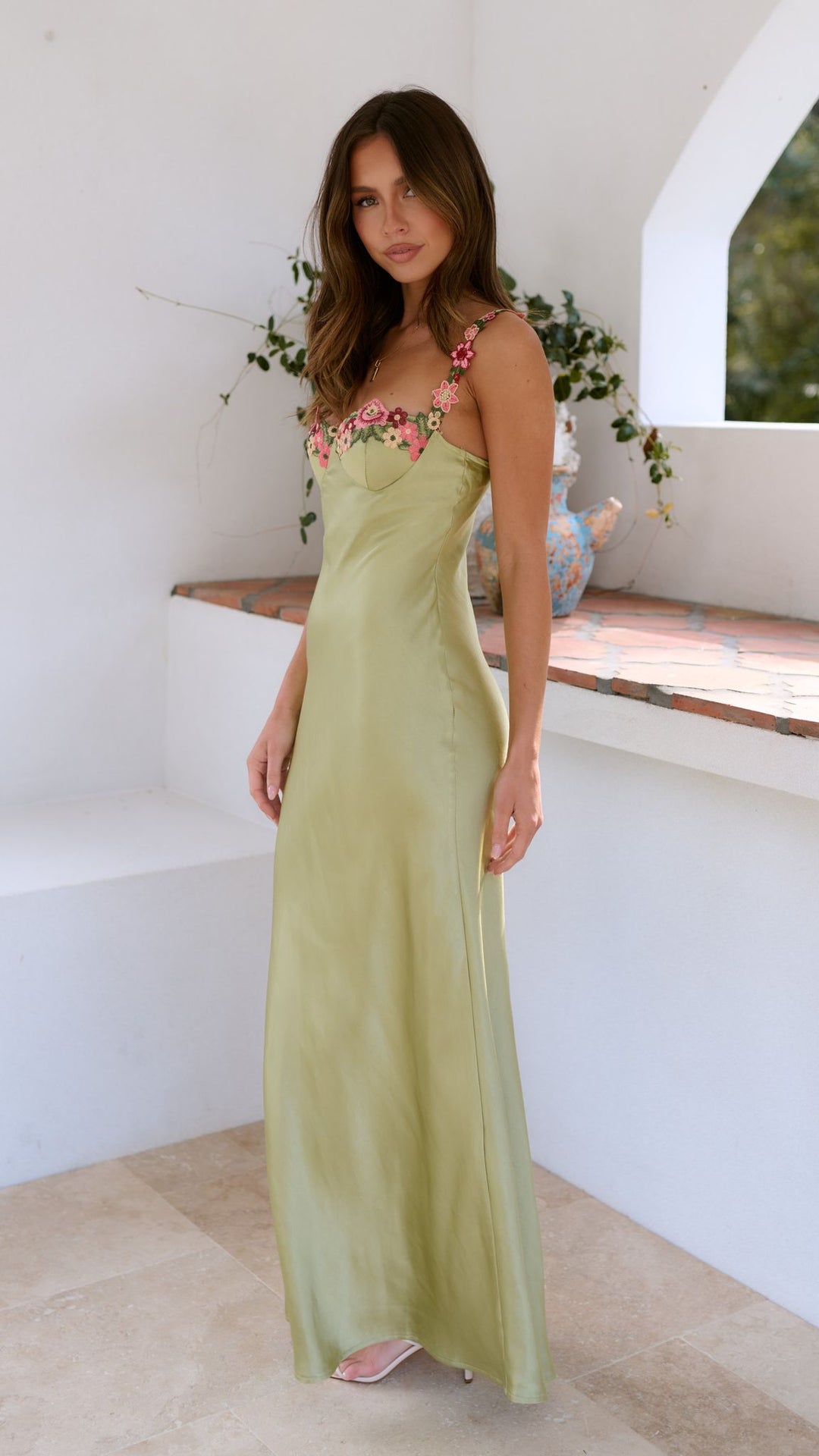 Woman wearing a light green dress with floral details in a bright room.