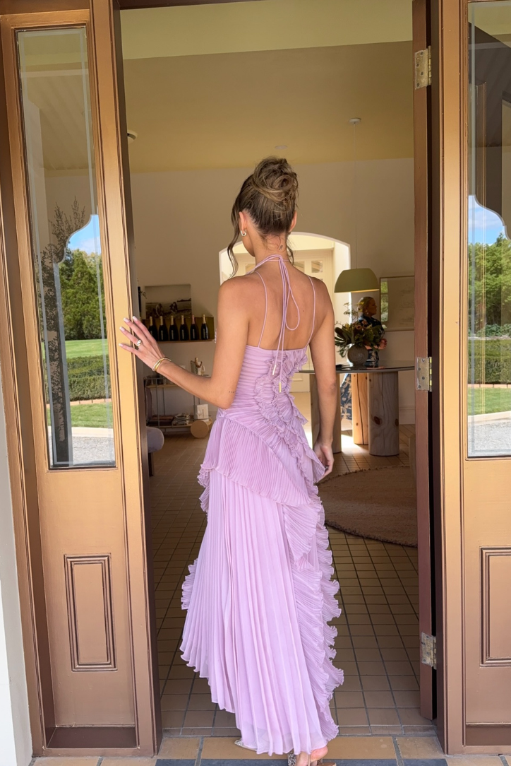 Woman in a purple dress standing in a doorway with a garden view.