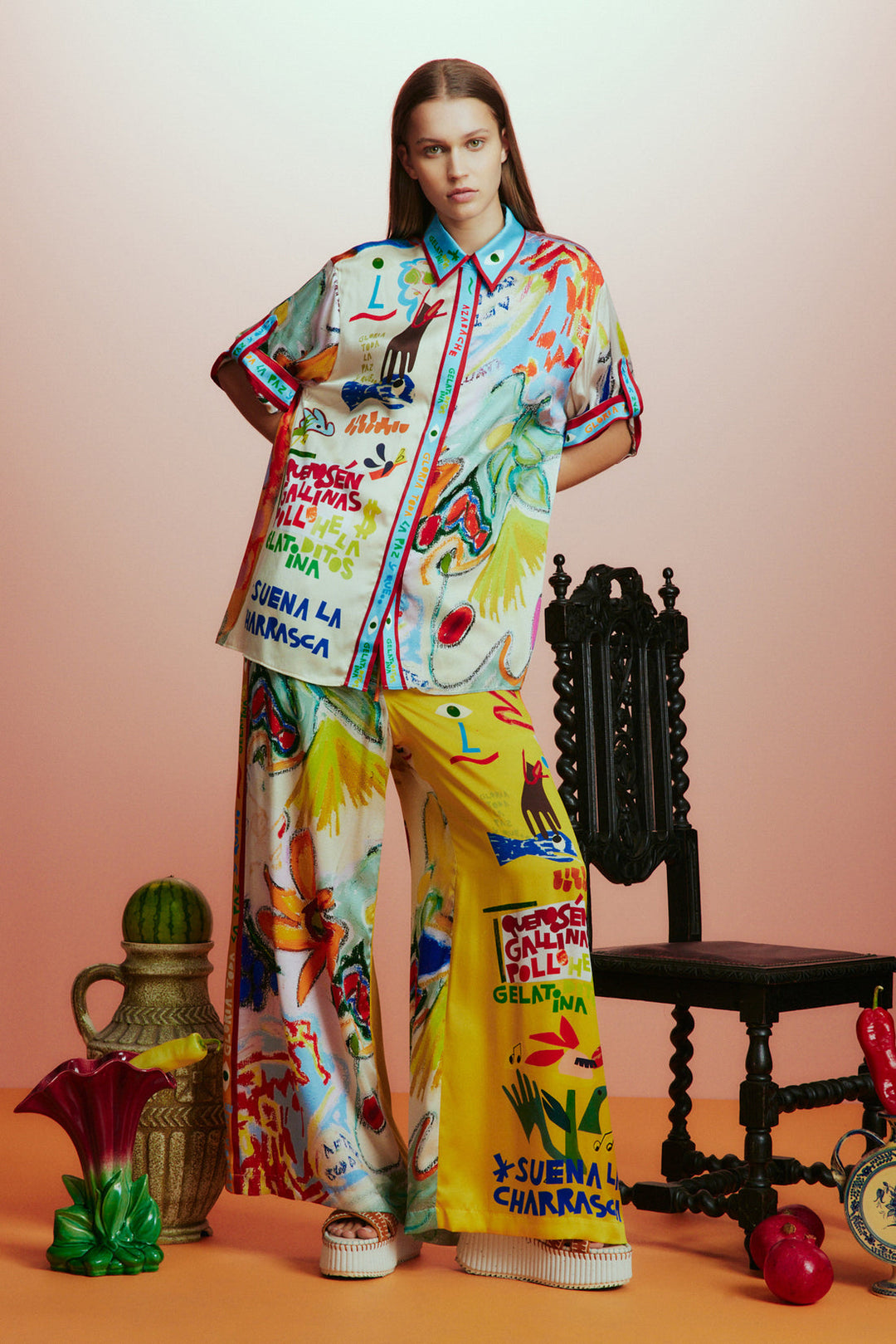 Model wearing a colorful outfit with text and graphics, standing against a gradient background.