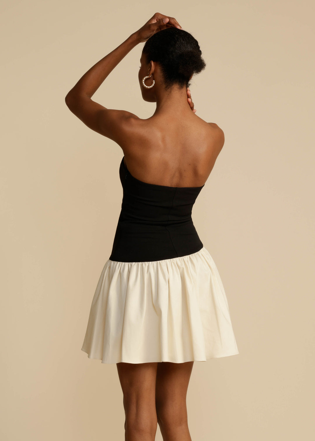 Woman wearing a black top and white skirt against a beige background