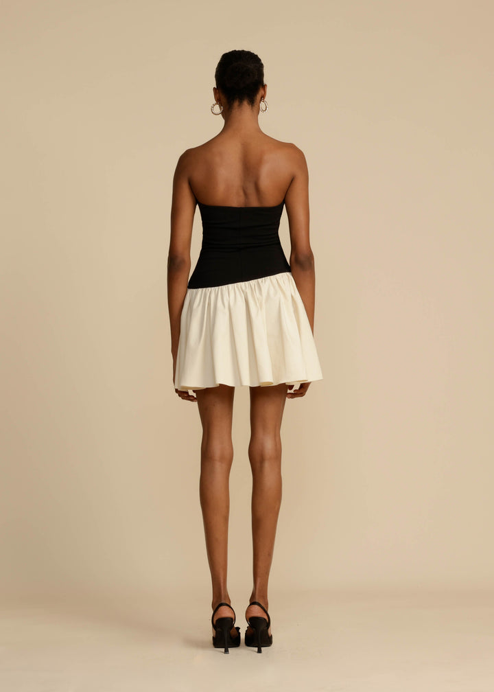 Woman wearing a black top and white skirt on a beige background
