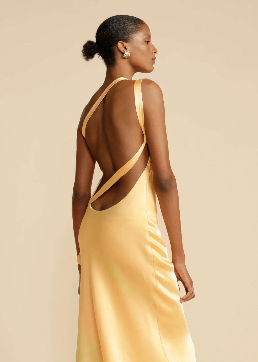 Woman wearing a yellow evening gown with open back on a beige background