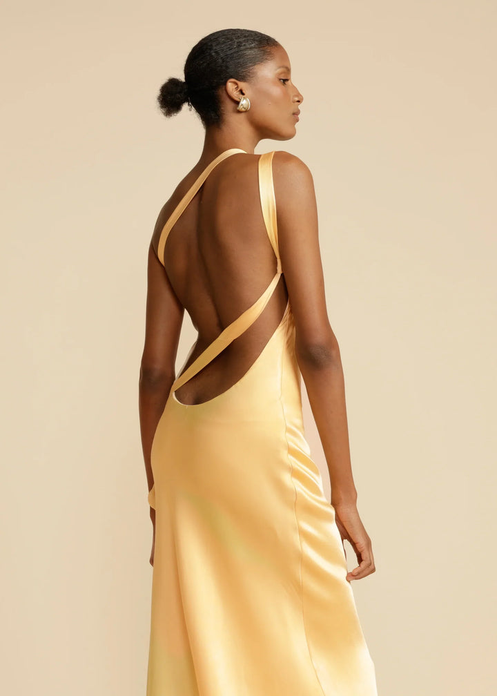 Woman wearing a yellow evening gown with open back on a beige background