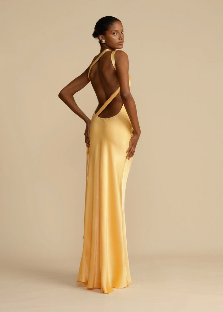 Woman wearing a gold evening gown with an open back against a beige background