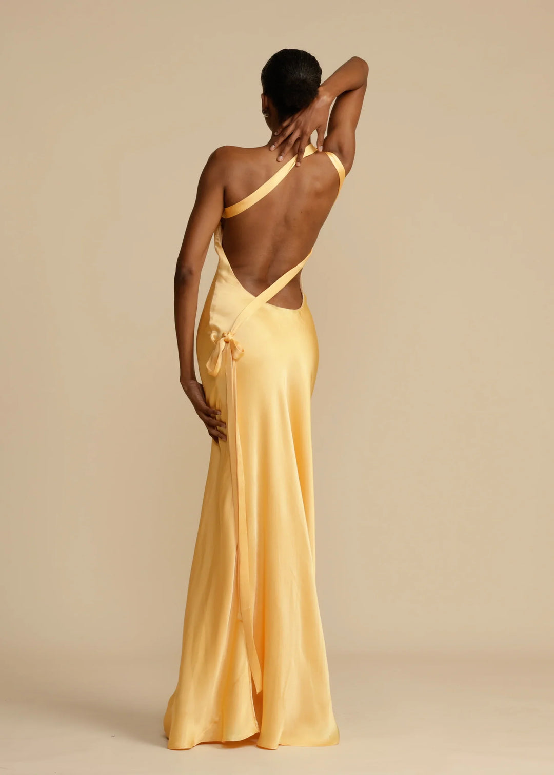 Woman wearing a long yellow dress with a backless design on a beige background