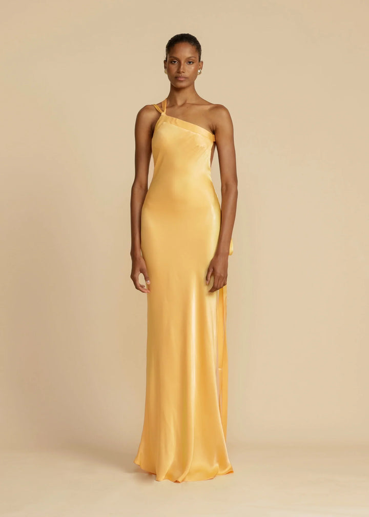Woman wearing a yellow satin one-shoulder gown against a beige background