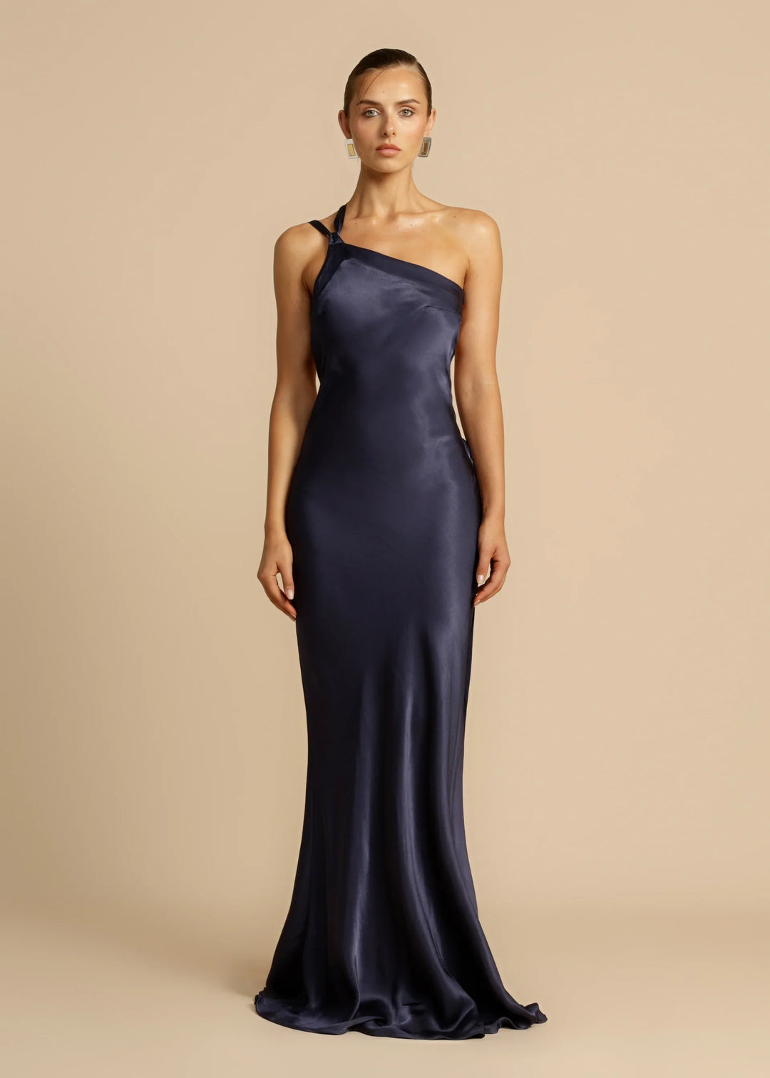 Woman wearing a one-shoulder navy gown against a beige background