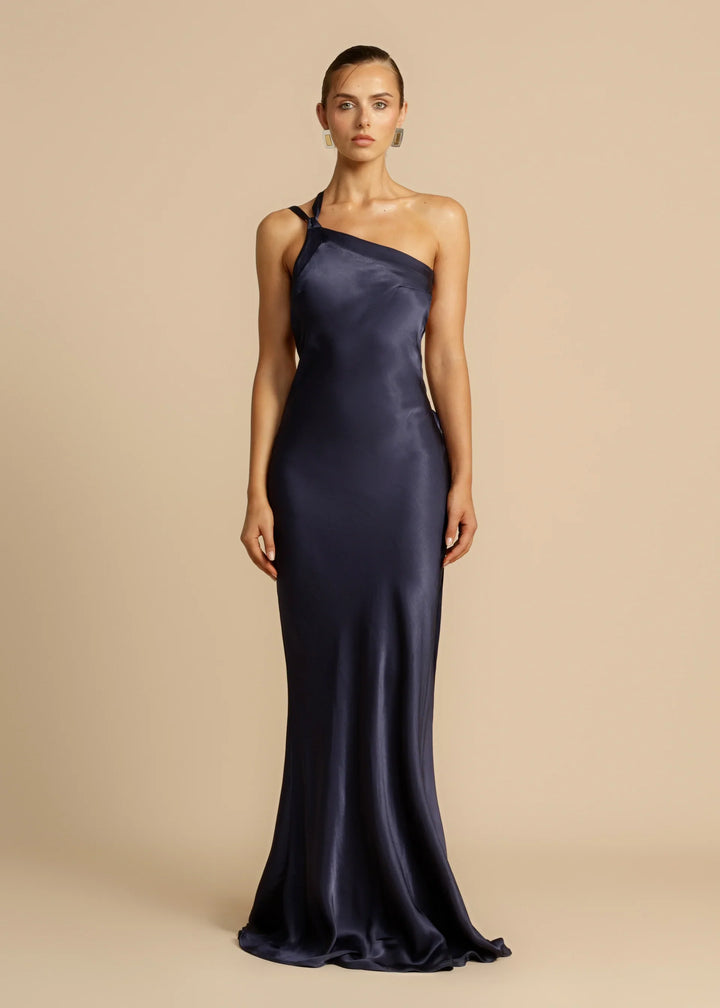 Woman wearing a one-shoulder navy gown against a beige background